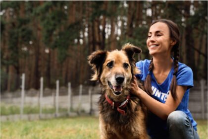 A woman in a blue shirt sitting with a dog outside a shelter and wondering, “What do you need to adopt a dog?”